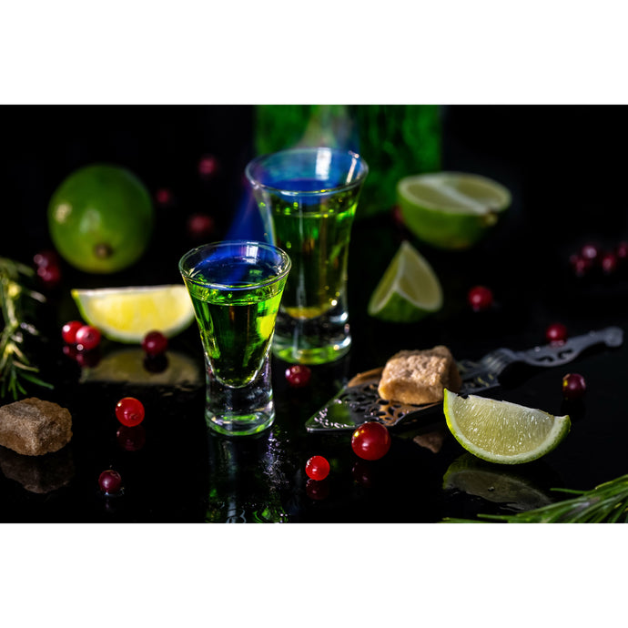 Shot glasses of green absinthe on black table with limes and currant berries