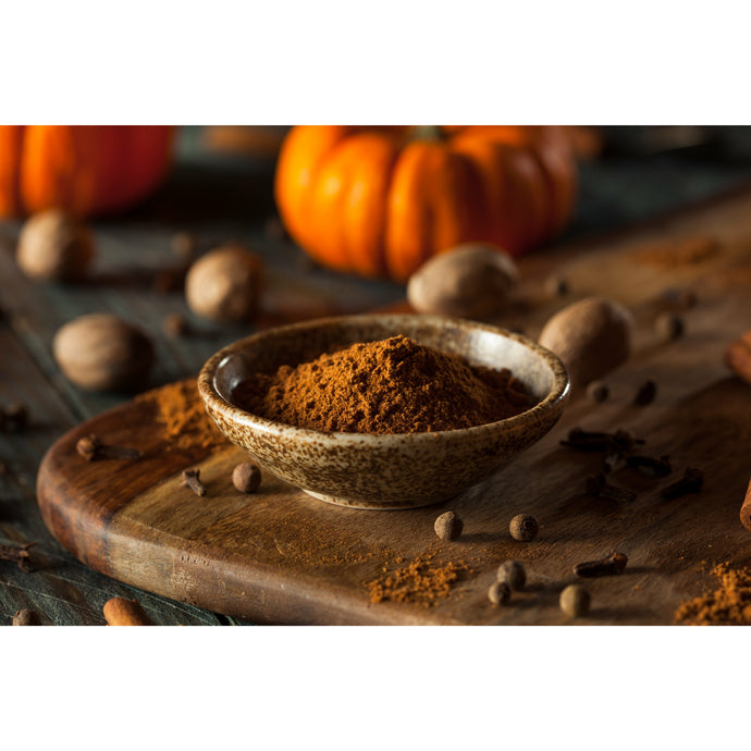 Pumpkin Spice image - Bowl of brown spice in ceramic bowl on cutting board with cloves, nuts and pumpkins in background.